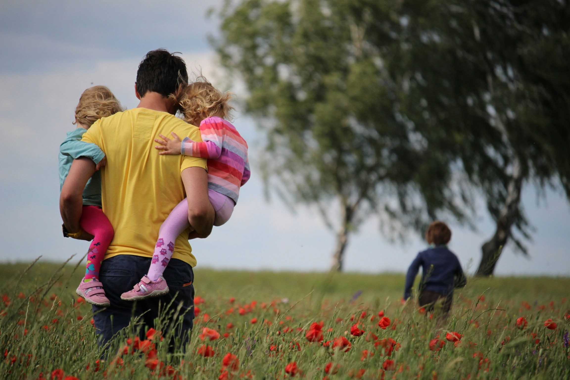 Father carrying two children through a poppy field